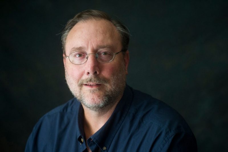 Dr. Bruce McComiskey sits for a headshot wearing a blue shirt against a dark backdrop.